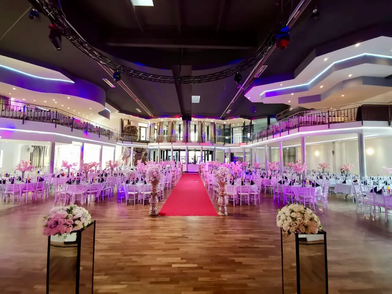 Großer Hochzeitssaal mit rotem Teppich, festlich eingedeckten Tischen und Bühne
